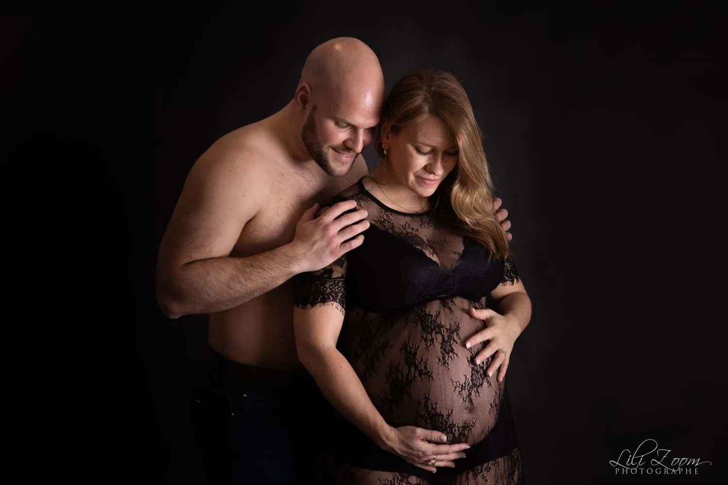 Un couple attend son bébé, le papa enlace la futur maman enceinte dans une robe de dentelle noire, shooting grosses dans le Calvados
