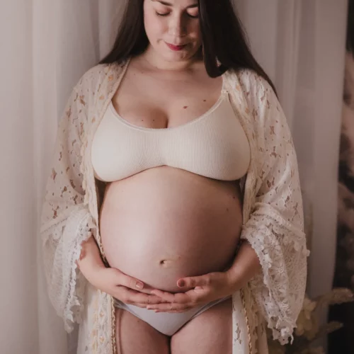 Une femme en dentelle caresse son ventre arrondi en attendant la naissance de bébé, shooting professionnel en studio bohème à Giberville