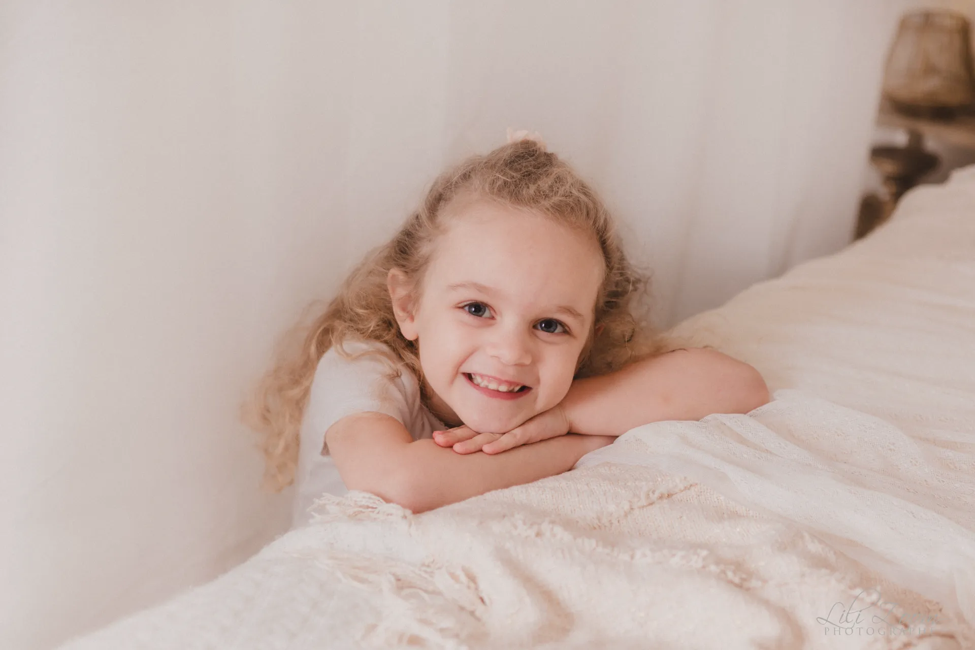 Petite fille aux cheveux bouclés souriant avec douceur dans un décor de studio épuré - Photographe Famille à Giberville