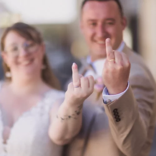 Couple de mariés complices et rock'n'roll montrant leurs alliances avec humour lors d'une séance décalée - Photographe Famille au Centre-ville de Caen