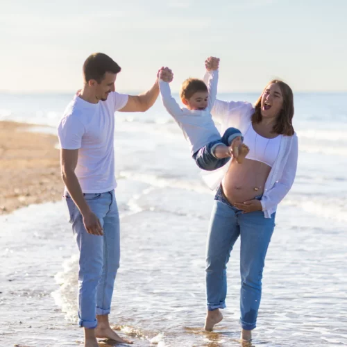 Moment de joie en famille avec les pieds dans l'eau pour une future maman et son jeune enfant - Photographe Grossesse à Ouistreham