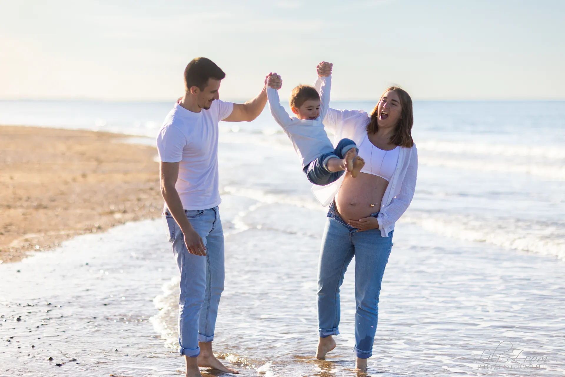 Moment de joie en famille avec les pieds dans l'eau pour une future maman et son jeune enfant - Photographe Grossesse à Ouistreham