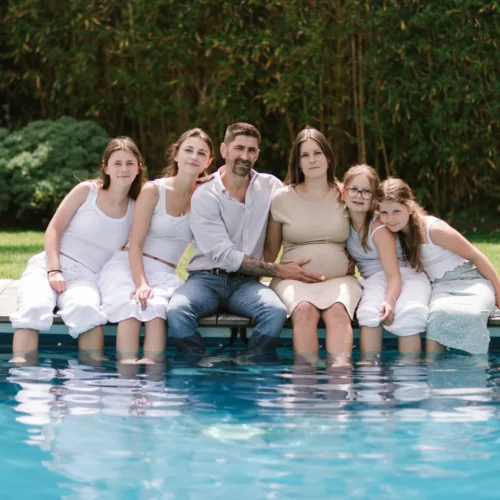 Famille recomposée assise au bord d'une piscine avec la maman enceinte - Photographe grossesse et famille Caen