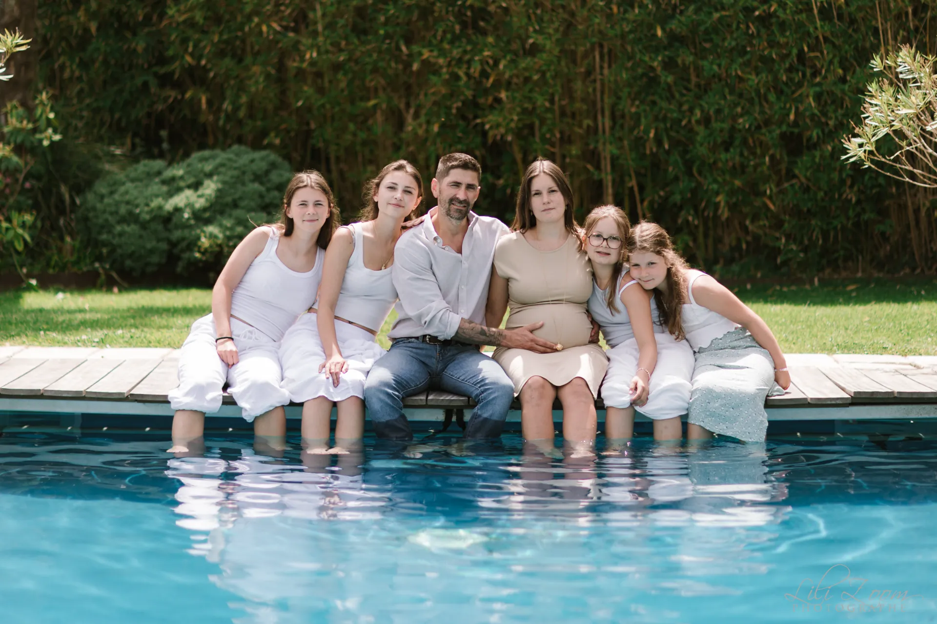 Famille recomposée assise au bord d'une piscine avec la maman enceinte - Photographe grossesse et famille Caen