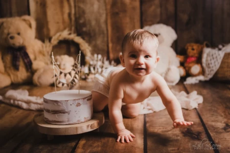 Petit garçon joyeux et malicieux rampant vers son gâteau d'anniversaire dans un décor rustique entouré d'ours en peluche - Séance Anniversaire au Studio à Giberville. Petit garçon joyeux et malicieux rampant vers son gâteau d'anniversaire dans un décor rustique entouré d'ours en peluche - Séance Anniversaire au Studio à Giberville.