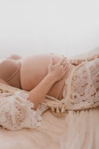 Détail du ventre arrondi d'une future maman allongée dans une tenue de dentelle délicate et bohème - Photographe Grossesse aux alentours de Colombelles Détail du ventre arrondi d'une future maman allongée dans une tenue de dentelle délicate et bohème - Photographe Grossesse aux alentours de Colombelles