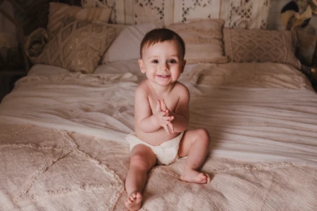 Adorable bébé souriant assis sur un lit dans un décor bohème et chaleureux - Photographe Bébé et Famille à Giberville Adorable bébé souriant assis sur un lit dans un décor bohème et chaleureux - Photographe Bébé et Famille à Giberville