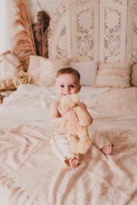 Portrait d'un bébé souriant tenant son doudou ours dans un décor bohème et chaleureux - Photographe Bébé et Famille à Giberville Portrait d'un bébé souriant tenant son doudou ours dans un décor bohème et chaleureux - Photographe Bébé et Famille à Giberville