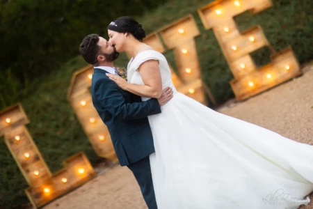 Baiser complice d'un couple de mariés devant des lettres géantes LOVE illuminées en plein air - Photographe Mariage et Famille à la Colline aux Oiseaux Baiser complice d'un couple de mariés devant des lettres géantes LOVE illuminées en plein air - Photographe Mariage et Famille à la Colline aux Oiseaux