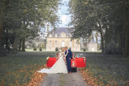 Couple de mariés s'embrassant tendrement devant une Coccinelle rouge vintage dans l'allée d'un château en automne - Photographe Famille à la Forêt de Bavent Couple de mariés s'embrassant tendrement devant une Coccinelle rouge vintage dans l'allée d'un château en automne - Photographe Famille à la Forêt de Bavent