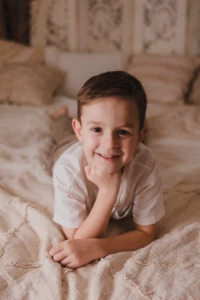 Portrait d'un petit garçon souriant et espiègle allongé sur un lit dans un décor studio doux et naturel - Photographe Famille proche de Colombelles Portrait d'un petit garçon souriant et espiègle allongé sur un lit dans un décor studio doux et naturel - Photographe Famille proche de Colombelles
