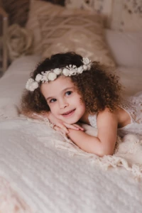Petite fille souriante aux cheveux bouclés portant une couronne de fleurs blanches sur un décor bohème - Photographe Famille aux alentours de Colombelles Petite fille souriante aux cheveux bouclés portant une couronne de fleurs blanches sur un décor bohème - Photographe Famille aux alentours de Colombelles