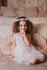 Petite fille aux cheveux bouclés portant une couronne de fleurs blanches dans un décor de studio doux et bohème - Photographe Famille à Giberville Petite fille aux cheveux bouclés portant une couronne de fleurs blanches dans un décor de studio doux et bohème - Photographe Famille à Giberville
