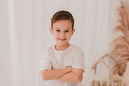 Portrait d'un petit garçon souriant les bras croisés dans un décor de studio lumineux et bohème - Photographe Famille à Giberville Portrait d'un petit garçon souriant les bras croisés dans un décor de studio lumineux et bohème - Photographe Famille à Giberville