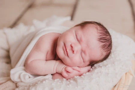 Nouveau-né paisible aux yeux clos esquissant un léger sourire, enveloppé dans un lange blanc sur un plaid texturé - Photographe Naissance à Giberville Nouveau-né paisible aux yeux clos esquissant un léger sourire, enveloppé dans un lange blanc sur un plaid texturé - Photographe Naissance à Giberville