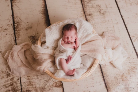 Nouveau-né paisiblement endormi et emmailloté dans un panier en osier sur un fond boisé rustique - Photographe Naissance à Giberville Nouveau-né paisiblement endormi et emmailloté dans un panier en osier sur un fond boisé rustique - Photographe Naissance à Giberville