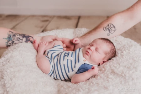 Nouveau-né paisiblement endormi sur un cocon de laine blanche, entouré par les mains protectrices et tatouées de ses parents - Photographe Naissance proche de Mondeville Nouveau-né paisiblement endormi sur un cocon de laine blanche, entouré par les mains protectrices et tatouées de ses parents - Photographe Naissance proche de Mondeville