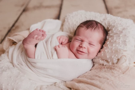 Nouveau-né paisible avec un léger sourire, emmailloté dans des voilages blancs sur un décor en bois naturel - Photographe Naissance secteur Mondeville Nouveau-né paisible avec un léger sourire, emmailloté dans des voilages blancs sur un décor en bois naturel - Photographe Naissance secteur Mondeville