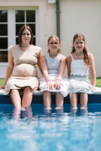 Femme enceinte avec ses deux filles assises au bord de la piscine - Photographe grossesse Mondeville Femme enceinte avec ses deux filles assises au bord de la piscine - Photographe grossesse Mondeville