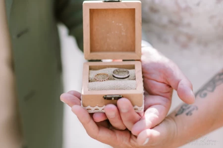 Alliances de mariage posées dans une petite boîte en bois tenue par les mains des mariés - Photographe mariage Honfleur Alliances de mariage posées dans une petite boîte en bois tenue par les mains des mariés - Photographe mariage Honfleur