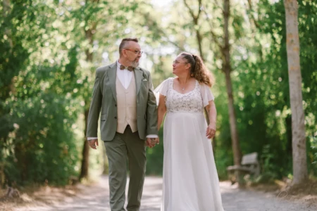 Couple de mariés se tenant la main en marchant sur un chemin boisé - Photographe mariage Bayeux Couple de mariés se tenant la main en marchant sur un chemin boisé - Photographe mariage Bayeux