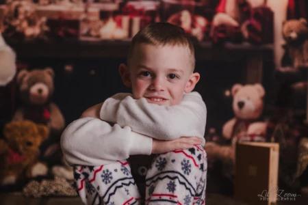 Jeune enfant assis devant un fond de peluches. Un jeune enfant assis, les bras entourant ses genoux, devant un fond rempli d’ours en peluche.