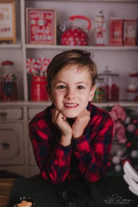 Un enfant pose devant une étagère décorative. Un enfant en chemise à carreaux rouge et noire pose devant une étagère décorée d’objets rouges et blancs, avec les mains sous le menton.